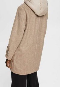 Beżowy płaszcz w jodełkę z odpinanym jasnobeżowym kapturem, bocznymi kieszeniami i zapinanymi na guziki rękawami, o prostym, luźnym kroju.