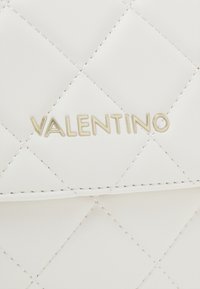 Borsa in pelle bianca trapuntata con logo dorato "Valentino", caratterizzata da un distintivo motivo a diamante e cuciture crema lungo i bordi.