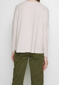 Ljust beige, texturerad långärmad topp med avslappnad passform och sänkta axlar, i kombination med olivgröna cargobyxor med sidofickor.