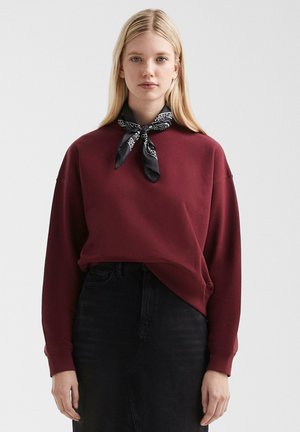 Sweat-shirt bourgogne avec un col rond et des épaules tombantes, associé à un bandana noir. Vêtements à la coupe décontractée et aux détails minimalistes.