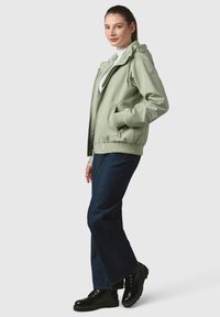 Jasnozielona kurtka z kapturem, zapinana na zamek, z bocznymi kieszeniami. Połączona z ciemnoniebieskimi spodniami typu wide-leg i czarnymi sznurowanymi botkami.