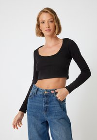 Top corto nero con maniche lunghe e scollo a barco, abbinato a jeans blu a vita alta con chiusura a bottone e tasche.