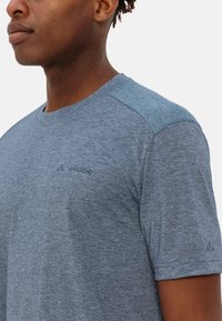 Camicia a maniche corte blu melange con accenti blu scuro sulle spalle e un logo discreto sul petto, realizzata in un tessuto testurizzato.