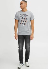 Camiseta de algodón gris con el texto "AIR FORCE" y un diseño gráfico colorido. Combinada con jeans oscuros y zapatillas multicolores.