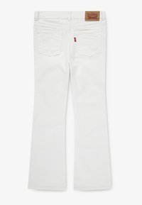 Jean en denim blanc évasés avec une étiquette de ceinture arborant un logo, deux poches plaquées au dos et des détails de couture contrastants.