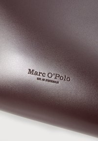 Mørkebrunt læderpung med præget "Marc O'Polo" logo og teksten "EST. IN STOCKHOLM". Glat tekstur med subtil glans.