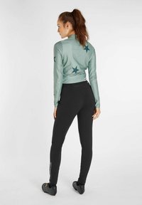 Jasnozielona bluzka z długim rękawem ozdobiona ciemnymi gwiazdkami, zestawiona z dopasowanymi czarnymi spodniami z suwakiem przy kostce i pewnym paskiem w talii.