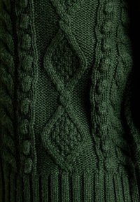Ciemnozielony sweter dzianinowy z misternymi wzorami, w tym kablami i diamentami, z ściągaczem na dole oraz różnymi teksturowanymi ściegami.