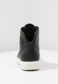 Schwarze Leder-Ankelboots mit runder Form, die eine kreisförmige Akzentuierung an der Seite und eine weiße Gummisohle aufweisen. Glatte Textur.