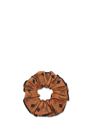 Chouchou en tissu marron avec des formes en losange noires et des logos "MCM" disposés en cercle sur un fond blanc.