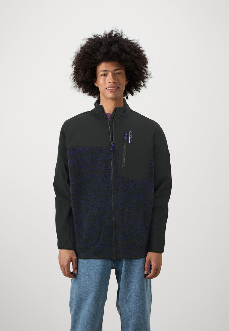 Giacca in fleece nera e blu scuro con chiusura a zip, colletto alto e tasca sul petto con un motivo a onde blu e branding.