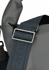 Borsa a spalla in pelle grigia con una tracolla strutturata caratterizzata da un motivo scuro. Una fibbia in metallo fissa la tracolla alla borsa, migliorandone la funzionalità.