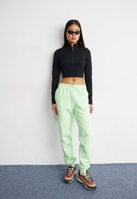 Crna uska zip-up majica u kombinaciji s svijetlim mentezama trenirkama i šarenim sportskim tenisicama. Glatke teksture i atletski dizajnerski elementi.