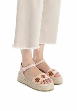 Sandalias de tela rosa bordadas con suela de yute en cuña. Presentan diseños florales en naranja y verde, con correa ajustable en el tobillo para un mejor ajuste.