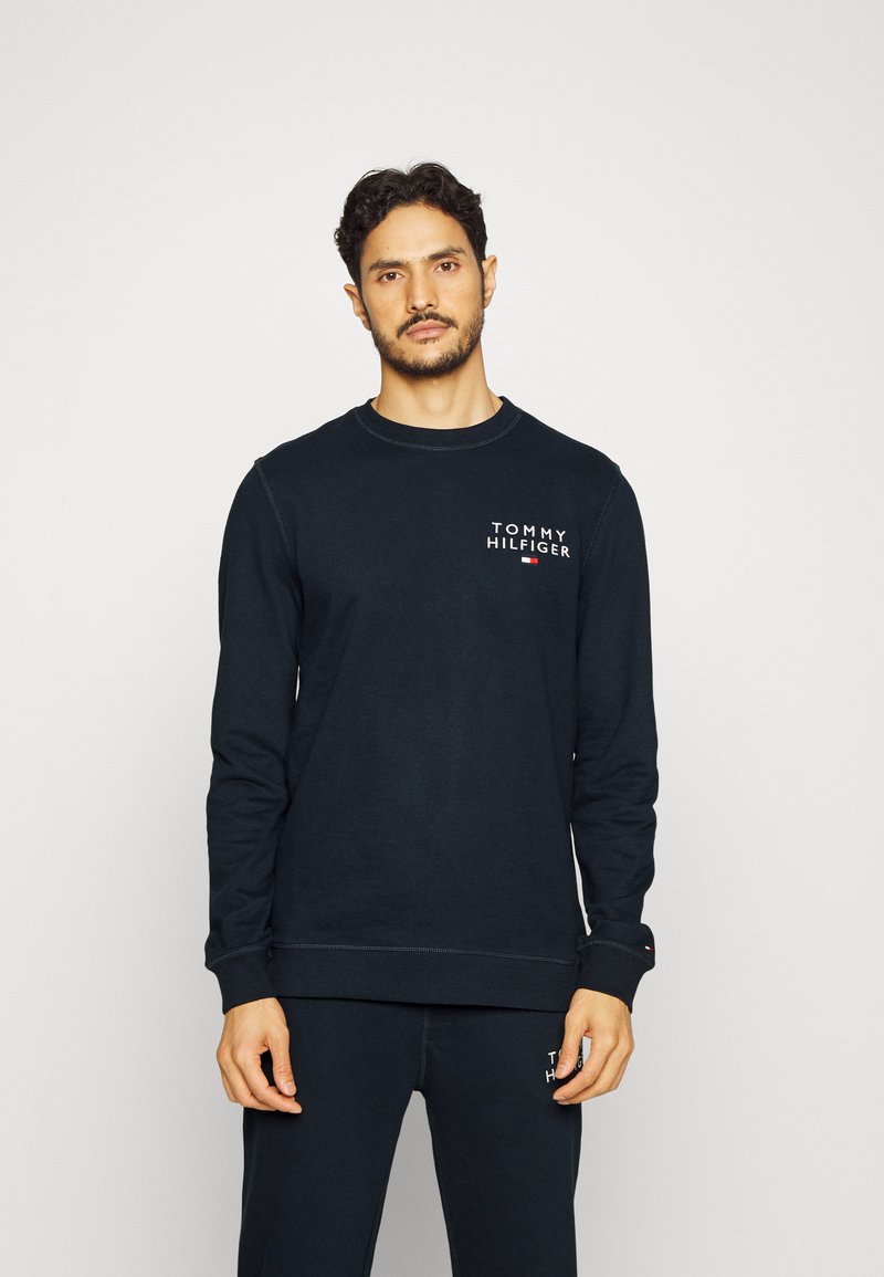 Sweatshirt bleu marine à manches longues, col rond et logo sur la poitrine, fabriqué dans un tissu doux. Pantalon assorti visible en dessous.