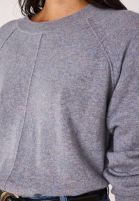 Maglione azzurro chiaro realizzato in morbido tessuto a maglia, con scollatura rotonda e maniche raglan. Mostra una texture fine e una leggera variazione di colore.