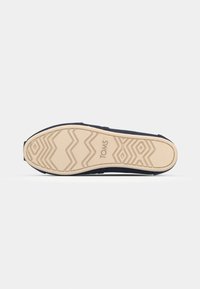 Semelle de chaussure avec une semelle en caoutchouc marron clair comportant des motifs en zigzag et en diamant, avec le logo "TOMS" embossé au centre.