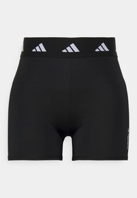 Mustat urheilushortsit, joissa on joustava vyötärönauha ja heijastava logo. Silkkinen kangas ja tiukka leikkaus. Ei taskuja tai lisäkuvioita.