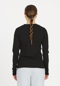 Schwarzes langärmliges Rippoberteil mit Rundhalsausschnitt und eng anliegenden Ärmeln. Getragen mit grauen Sweatpants und einer geflochtenen Frisur.
