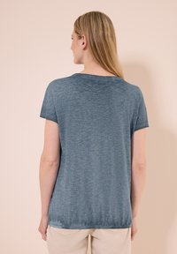T-shirt blu a maniche corte con vestibilità comoda, scollo rotondo e texture morbida. Il retro presenta un bordo leggermente curvo.