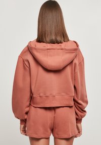 Rosenroze cropped sweatshirt met capuchon en brede mouwen, gecombineerd met bijpassende korte broek. Stof oogt zacht met minimale naden.