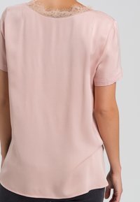 Blouse à manches courtes en satin rose clair, avec une finition en dentelle texturée au niveau de l'encolure. Surface lisse avec une coupe décontractée et un ourlet arrondi.