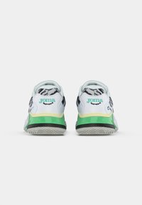 Baskets blanches avec une semelle verte et noire, présentant un motif zèbre sur le talon et une marque turquoise à l'arrière.