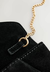 Black suede handbag with a smooth texture, featuring a gold metal chain strap and a metal ring and leather tab detail.