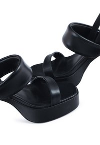 Sandalias de plataforma negras con correas anchas y curvadas y una textura de cuero suave. Presentan una base gruesa y sólida para mayor estabilidad.