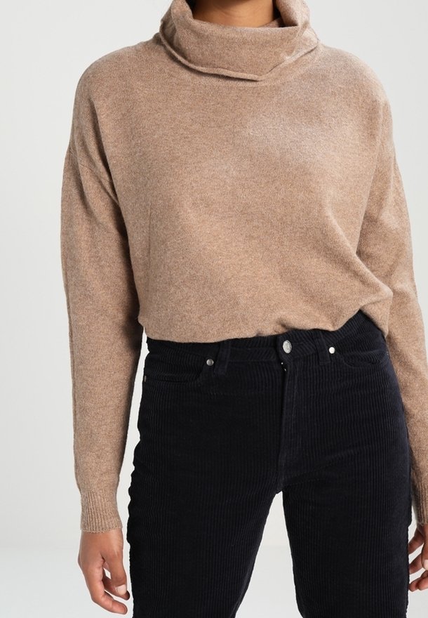 Beige, gebreide trui met een hoge, opgestikte kraag. Gecombineerd met aansluitende, donkere corduroy broek, met een knoop- en ritssluiting.
