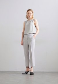 Top senza maniche grigio chiaro abbinato a pantaloni grigio chiaro. Tessuto morbido, vestibilità sartoriale, pantaloni alla caviglia, e tacchi neri con cinturino alla caviglia.