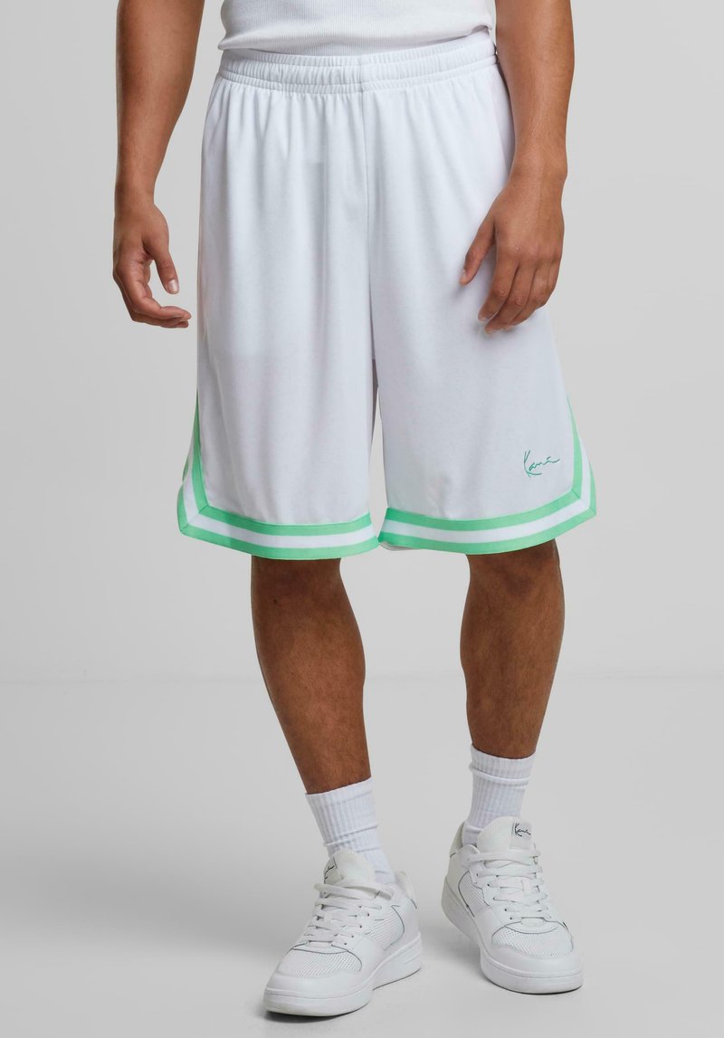 Shorts de sport blancs avec des accents en bandes vertes, taille élastique, texture lisse, longueur genou, avec un logo sur le côté inférieur gauche.