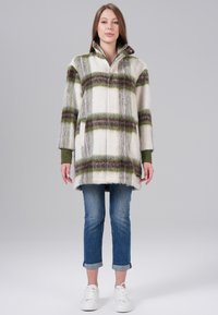 White plaid coat with green and brown stripes, made of textured fabric. Features a high collar and two side pockets. Paired with rolled jeans and white sneakers.