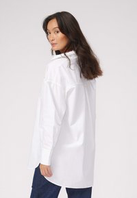 Hvid langærmet skjorte lavet af bomuld, med en button-down krave, afslappet pasform og rundet kant. Glat tekstur uden mønstre.