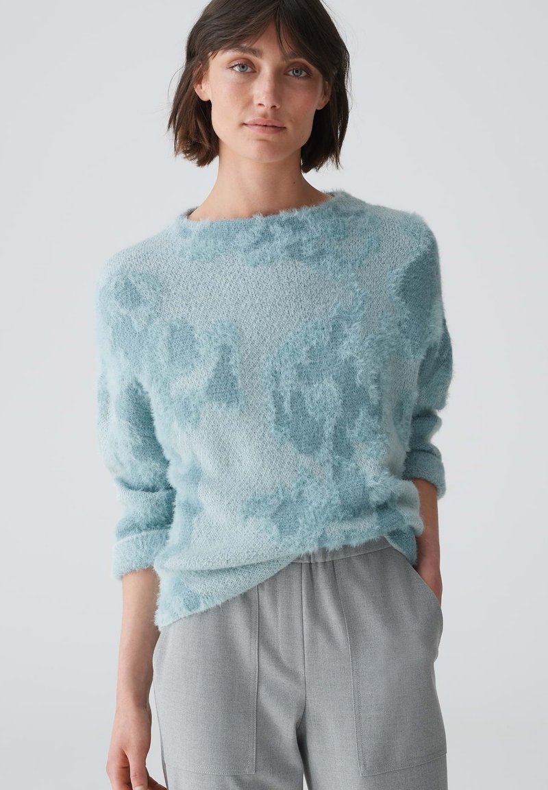 Helles blaues, flauschiges Sweatshirt mit lockerer Passform, rundem Ausschnitt und weicher Textur. Das Design weist subtile Farbvariationen und sanfte Akzente auf.