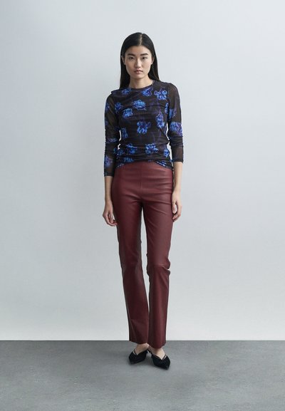 Long-sleeve transparent top with blue floral pattern paired with burgundy fitted pants and black flats, set against a neutral background.