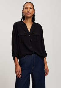 Czarna koszula z długim rękawem, z kołnierzykiem zapinanym na guziki, dwiema kieszeniami na piersi oraz metalowymi akcentami guzików. Połączona z ciemnoniebieskimi spodniami z wysokim stanem.