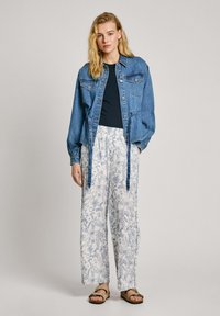 Veste en denim avec deux poches poitrine, pantalons large à motifs floraux bleus et top noir ; présente une coupe décontractée et des détails de taille nouée.
