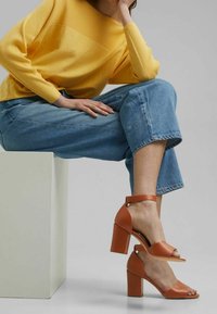 Sandales à talons hauts orange clair avec bout ouvert et bride de cheville, présentant une finition en cuir texturé et un talon carré épais.