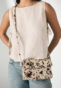 Beige linen top with side tie details, paired with a cream and brown speckled crossbody bag. Straight-leg blue jeans complete the outfit.