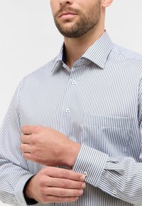Camicia button-up con sottili righe blu e bianche, colletto a punta e tasca sul lato sinistro, realizzata in cotone morbido.