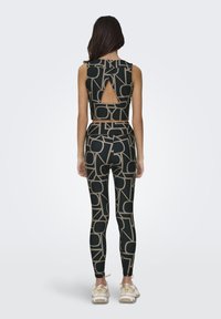 Zwarte cropped top met een keyhole achterkant en geometrisch beige patroon, gedragen met bijpassende taille hoge legging die hetzelfde ontwerp heeft.