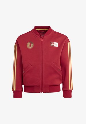 Red zip-up jacket made of sweatshirt material. Features yellow stripes on sleeves, side pockets, and a gold Mickey Mouse patch on chest.