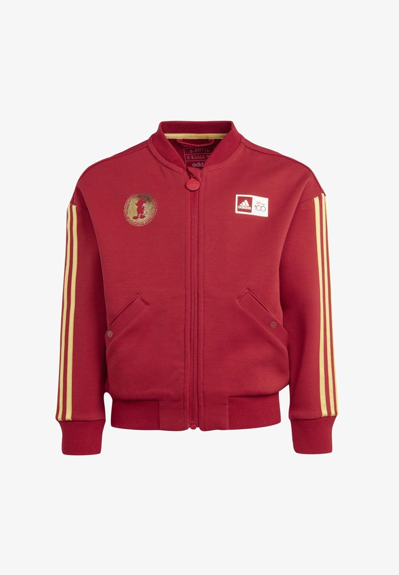 Czerwona kurtka zapinana na zamek, wykonana z materiału dresowego. Posiada żółte paski na rękawach, kieszenie po bokach oraz złotą naszywkę z Miki Mouse na klatce piersiowej.