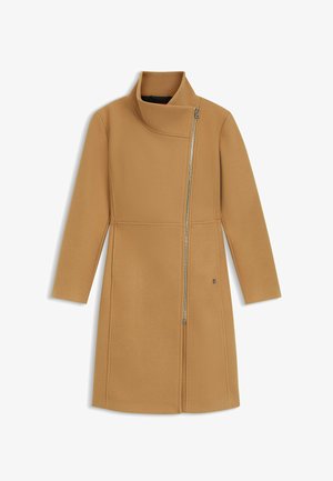 Lang jas in kameelkleur met asymmetrische zilveren ritssluiting die loopt van de kraag naar de rechterbenedenkant, voorzien van een hoge, opgevouwen kraag.
