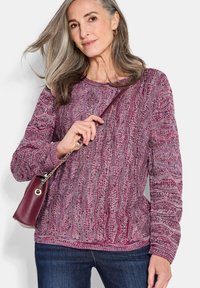 Maglione a maglia in un motivo melangiato bordeaux e rosa, con scollatura rotonda e maniche lunghe, abbinato a una borsa piccola.
