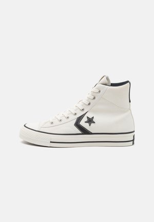 High-top sneakers made of white canvas with a black star logo and accent, featuring black sole stripes and round toe design.