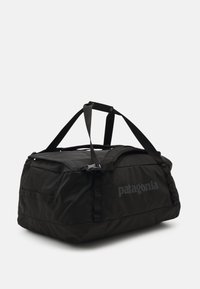 Black duffel bag with a rectangular shape, made from durable fabric. Features adjustable straps and a logo on the side. Simple, functional design.