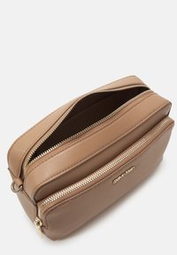 Brązowa skórzana kosmetyczka z dwiema zamykanymi na zamek przegrodami, złotymi detalami i logo Calvin Klein z przodu. Gładka tekstura.