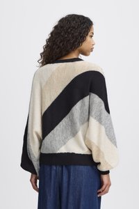 Pull surdimensionné avec des rayures diagonales en noir, crème, gris et beige. Texture tricotée avec des manches larges et un ourlet côtelé.
